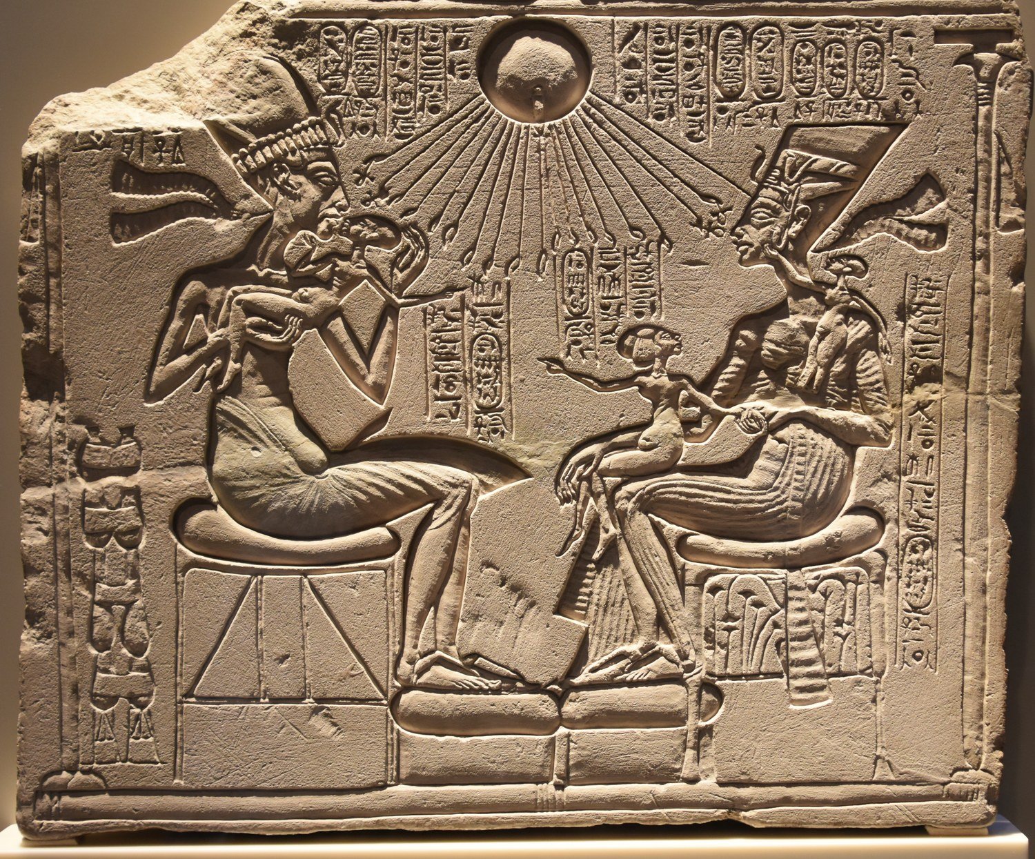 An Amarna relief of Akhenaten's family beneath the Aten — the sun-disk whose rays end in small human hands reaching down to touch the heads of the royal family